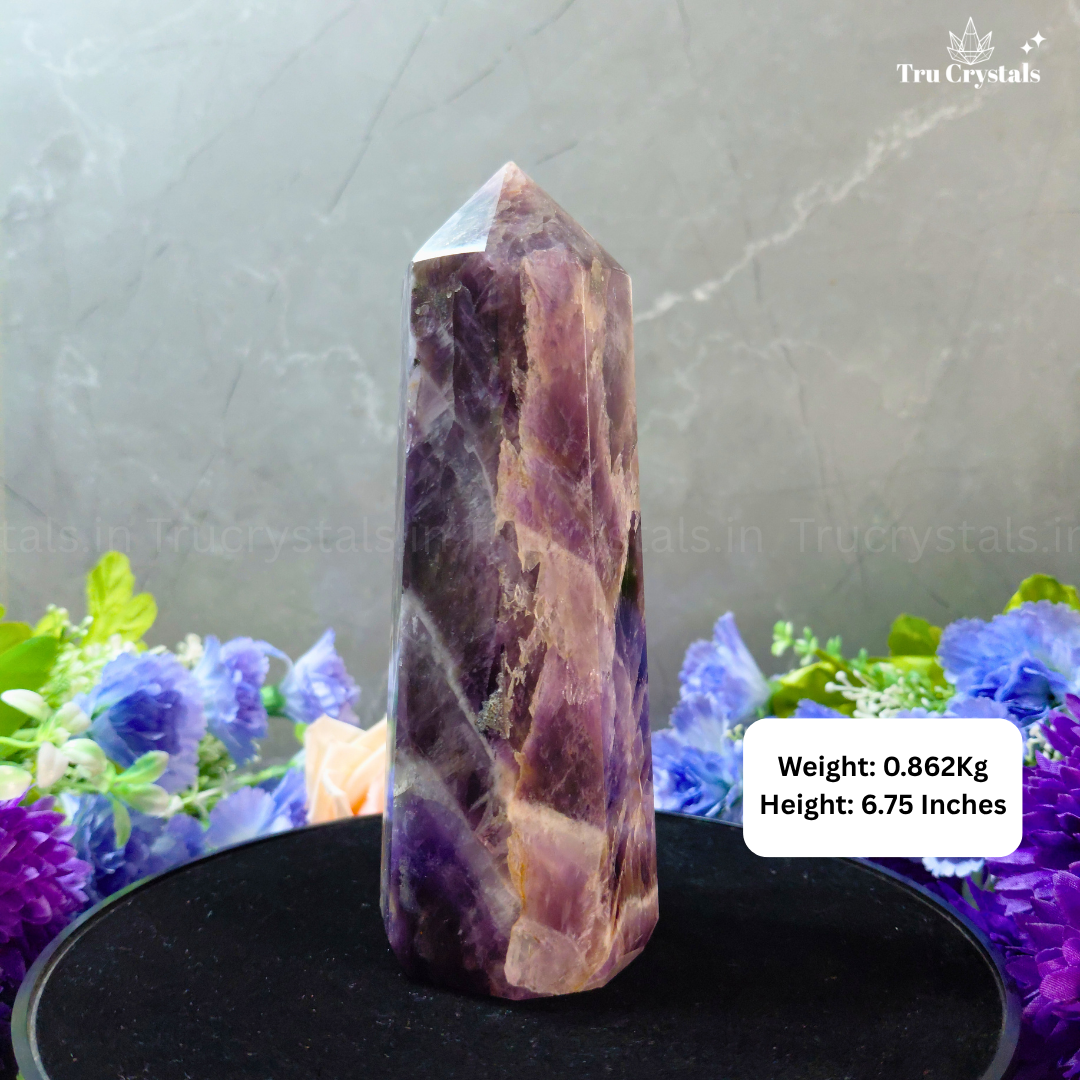 Purple crystal tower on a black stand with flowers in the background, branded 'Tru Crystals'.