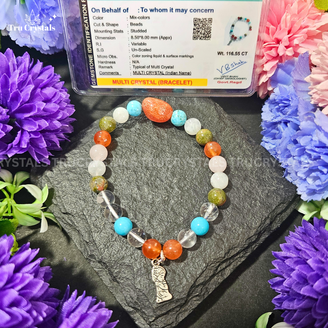 A multicolored stone bracelet with a combination of round and possibly square-shaped beads, displayed on a textured surface with purple and pink flowers in the background.