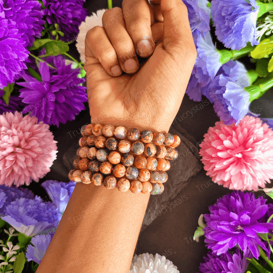 Fire agate bracelet to ignite passion is displayed on wrist of a person along with artificial flowers.