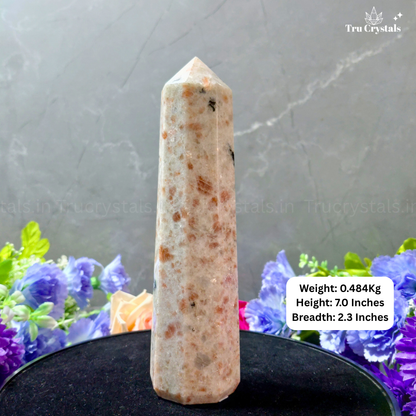 Sunstone crystal tower with weight, height, and breadth information on a gray background with flowers.