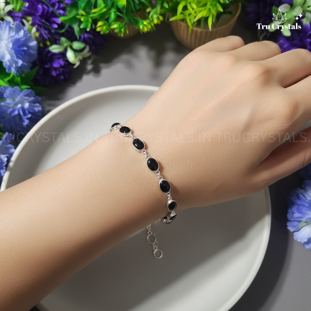 Silver bracelet with black tourmaline beads on a wrist, surrounded by flowers and plants.