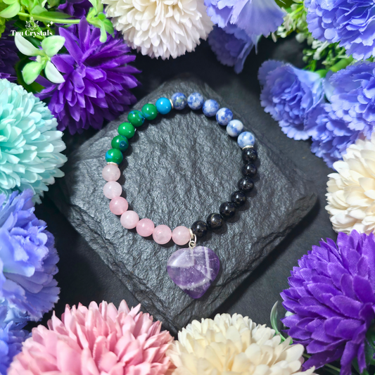 A multi beaded anger and irritability support bracelet made of various stones like rose quartz , black tourmaline, sodalite , chrysocholla, featuring a prominent amethyst pendant, displayed on a dark stone surface with flowers in the background