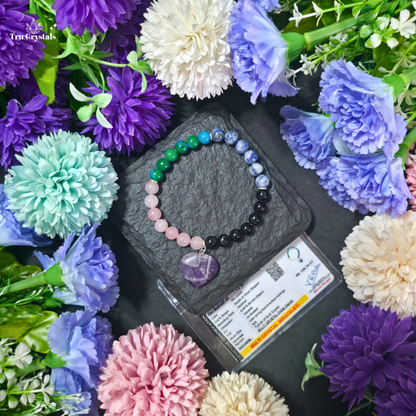 A beaded chakra bracelet with a purple amethyst pendant, displayed on a dark slate block next to a certification card. The bracelet features pink, green, blue, and black beads.