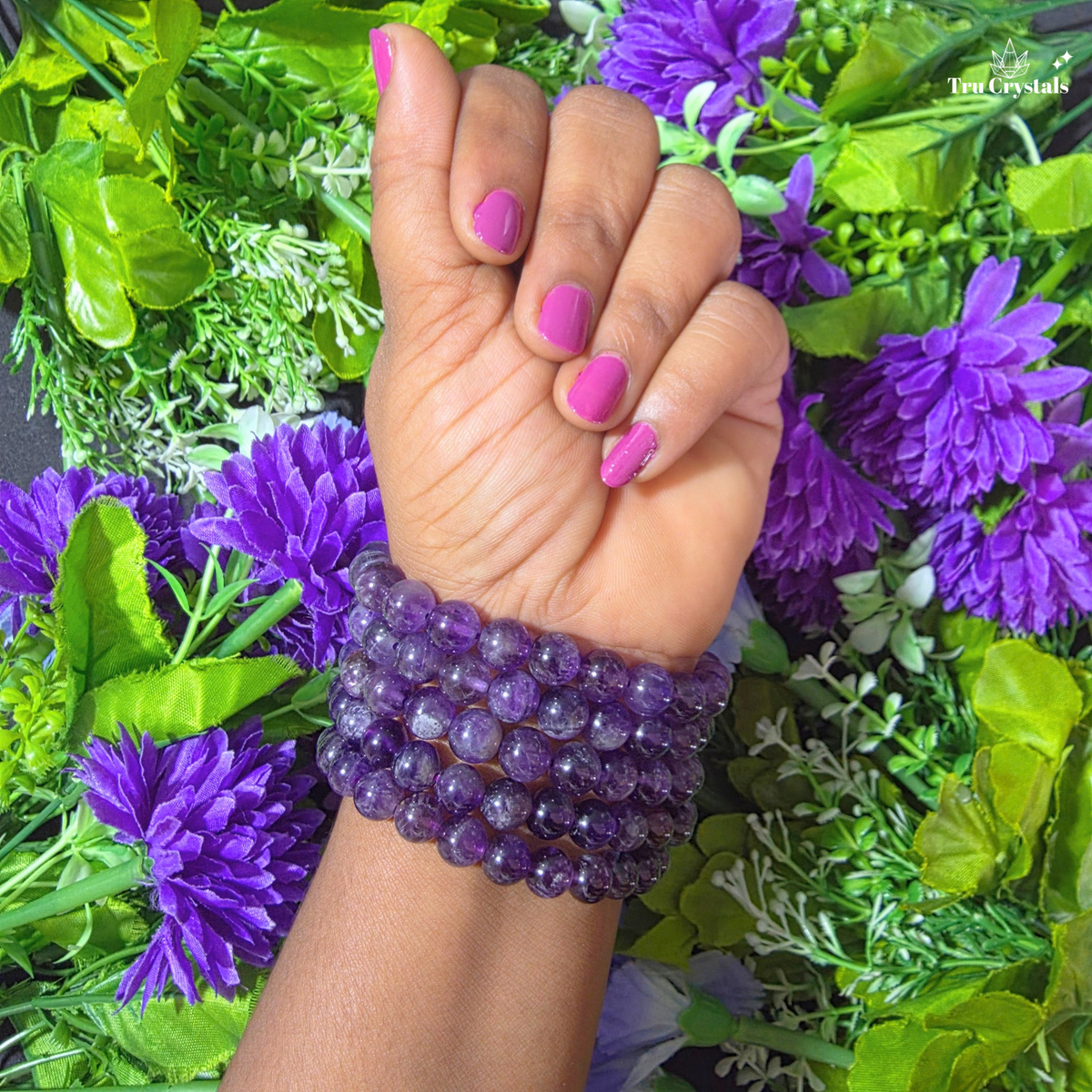 A purple amethyst chevron bracelet displayed on a white platform with a floral patterned backdrop, showcasing round gemstones linked together