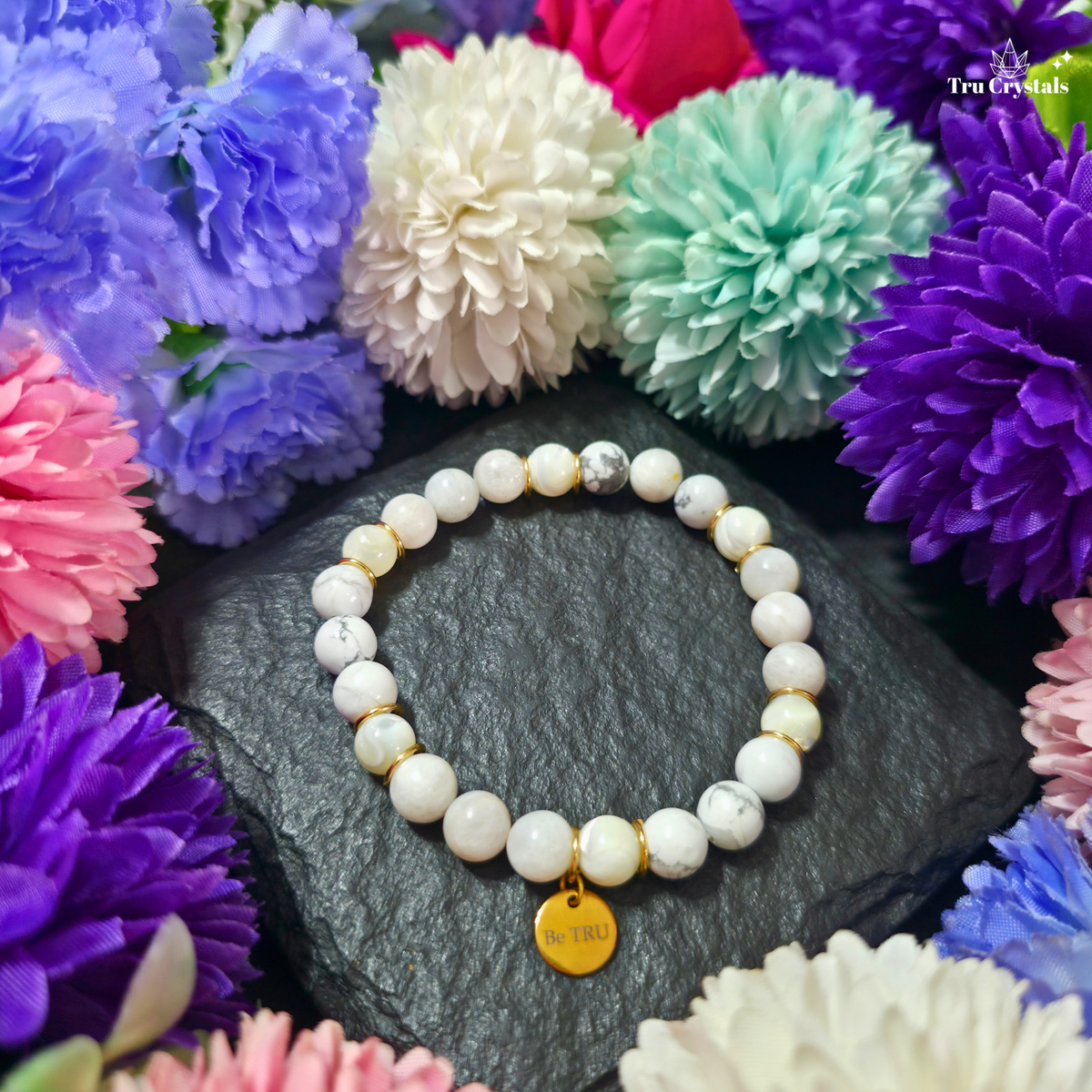 A bracelet conataining moonstone  , howlite and selenite for Numerology Bracelet Number 2 and moon having a be tru charm with a dark background. 