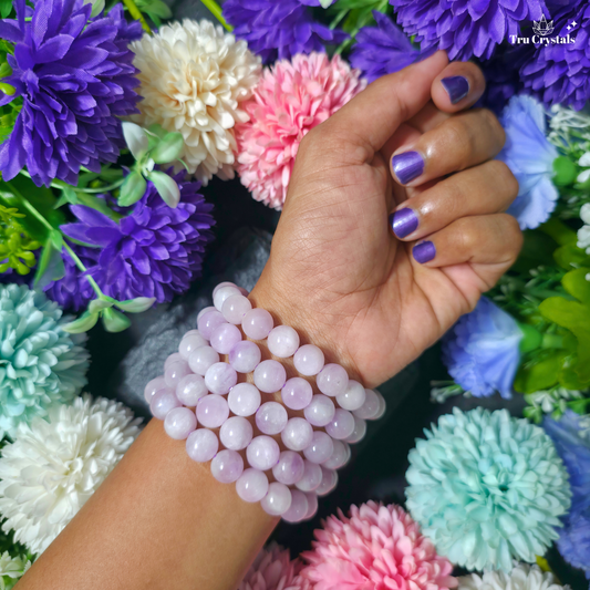 A handmade high quality Kunzite bracelet displayed on a dark background with artificial flowers.