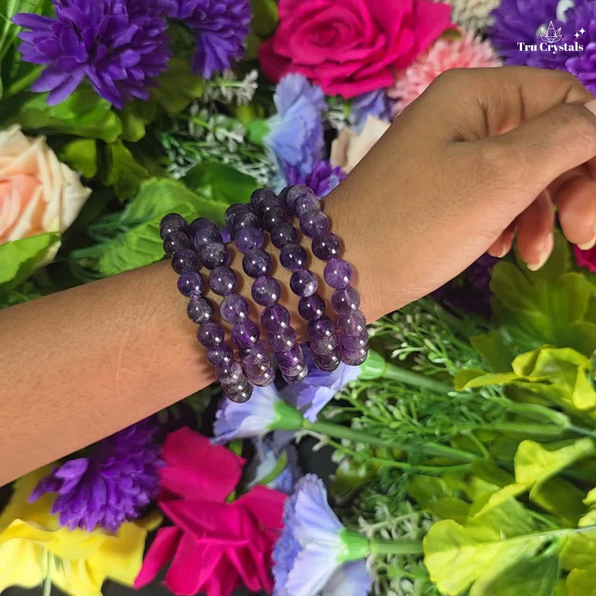 A purple amethyst chevron bracelet displayed on a white platform with a floral patterned backdrop, showcasing round gemstones linked together