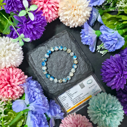 K2 Jasper bracelet placed on a dark surface, with certficate and 'Trucrystals' logo displayed surrounded by colorful flowers.