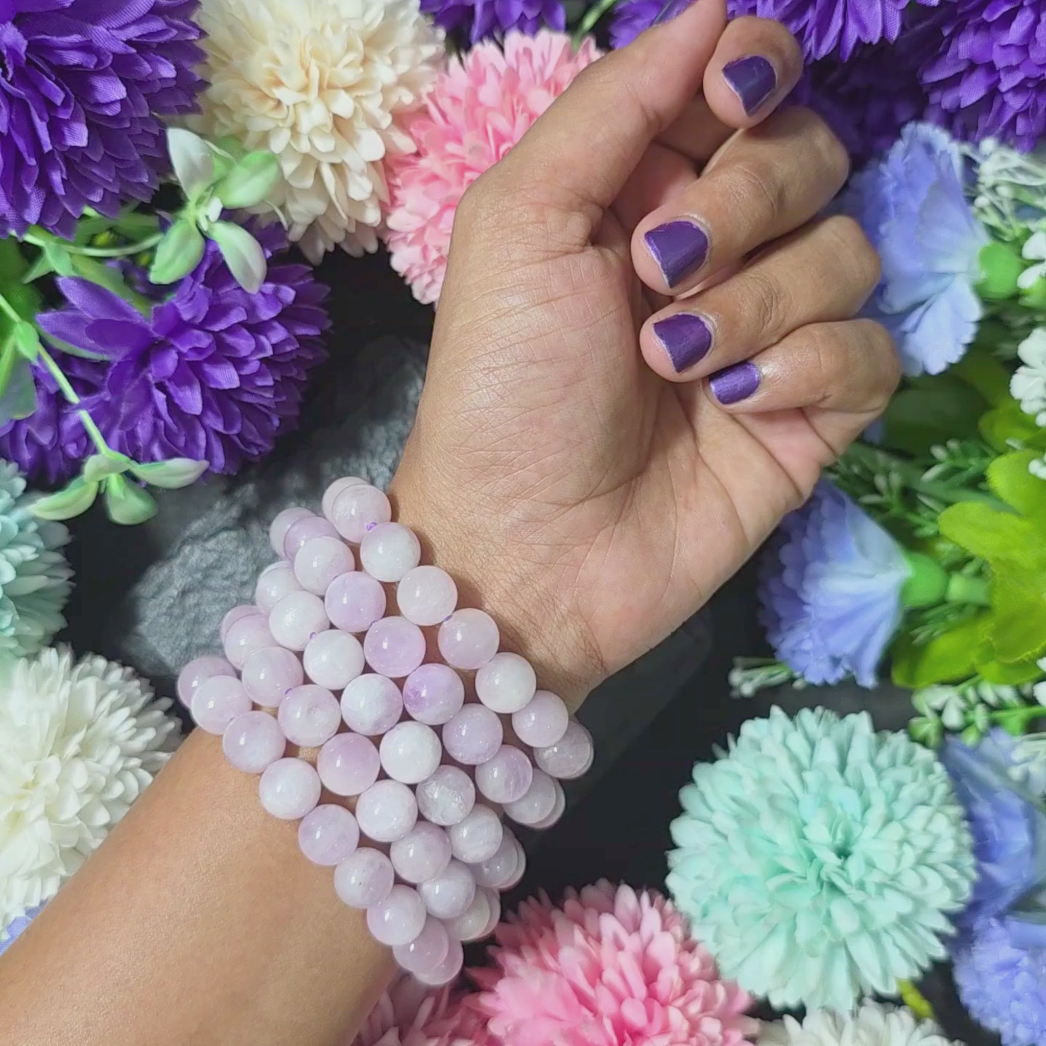 A handmade high quality Kunzite bracelet displayed on a dark background with artificial flowers.