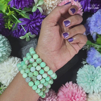 A bracelet featuring a series of round Chrysoprase gemstones on a stretch cord, displayed on a dark background .