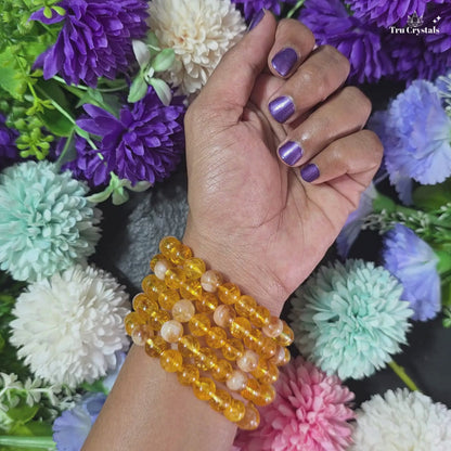 A CITRINE BRACELET  video displayed on a dark stone surface, surrounded by colorful flowers.