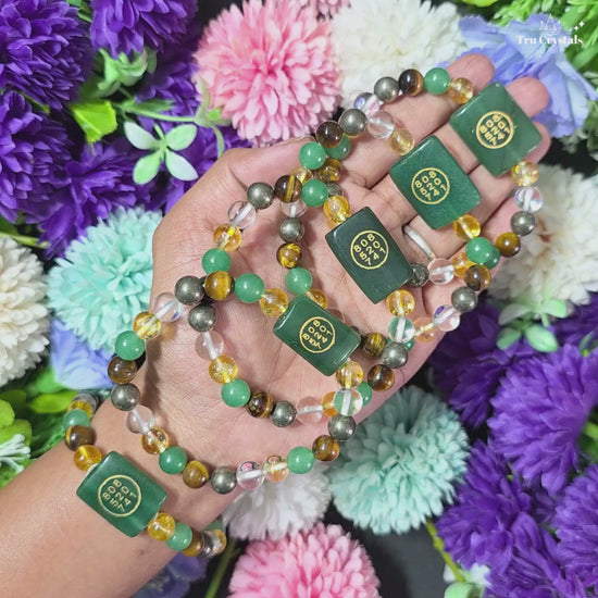 A person's wrist wearing an abundance bracelet with green and yellow gemstones and a zibu coin charm.