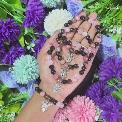 A multicolored stone  Soulmate bracelet displayed with a small heart-shaped pendant hanging from the bracelet. The bracelet contains rose quartz , Rhodonite , rhodochrosite & garnet .