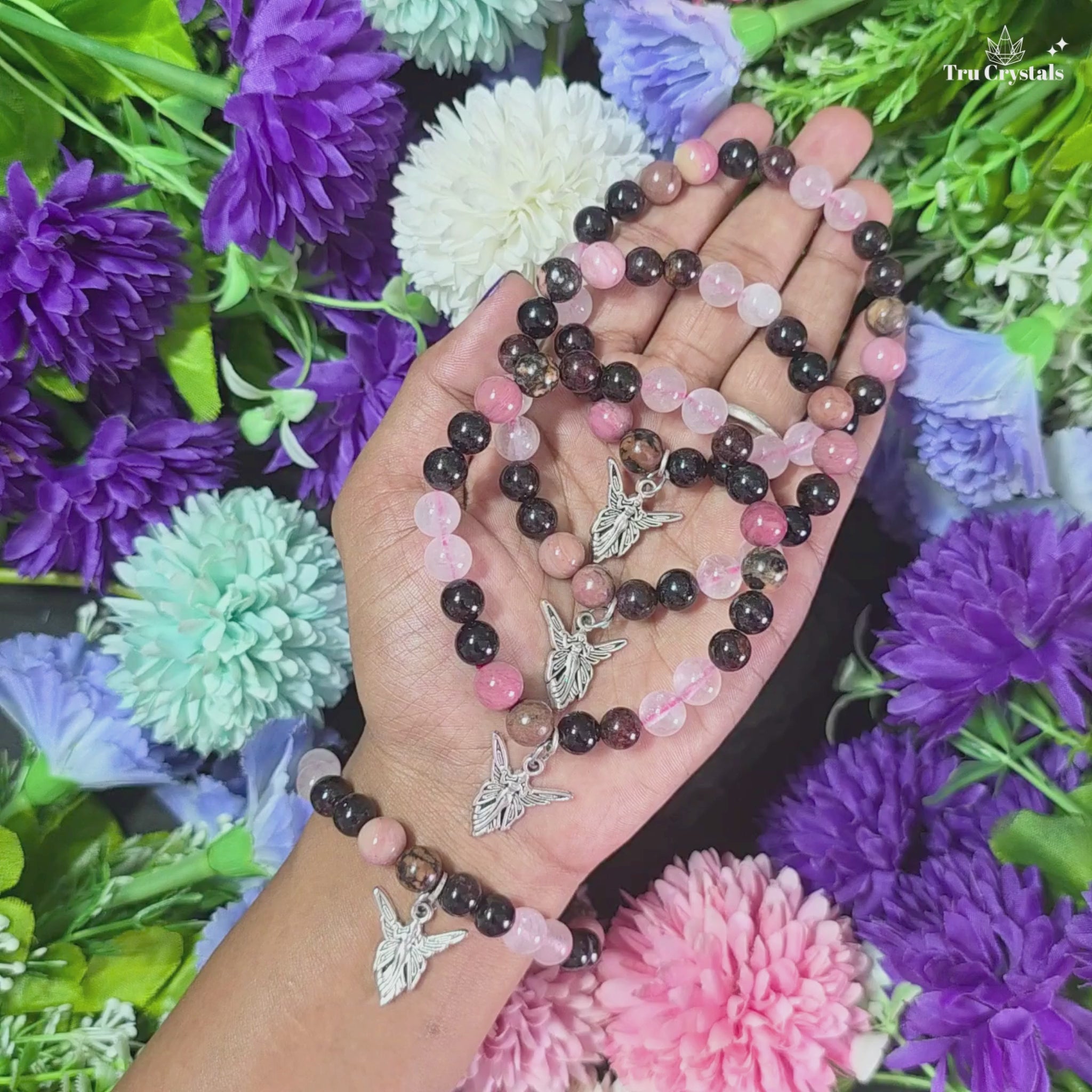 A multicolored stone  Soulmate bracelet displayed with a small heart-shaped pendant hanging from the bracelet. The bracelet contains rose quartz , Rhodonite , rhodochrosite & garnet .