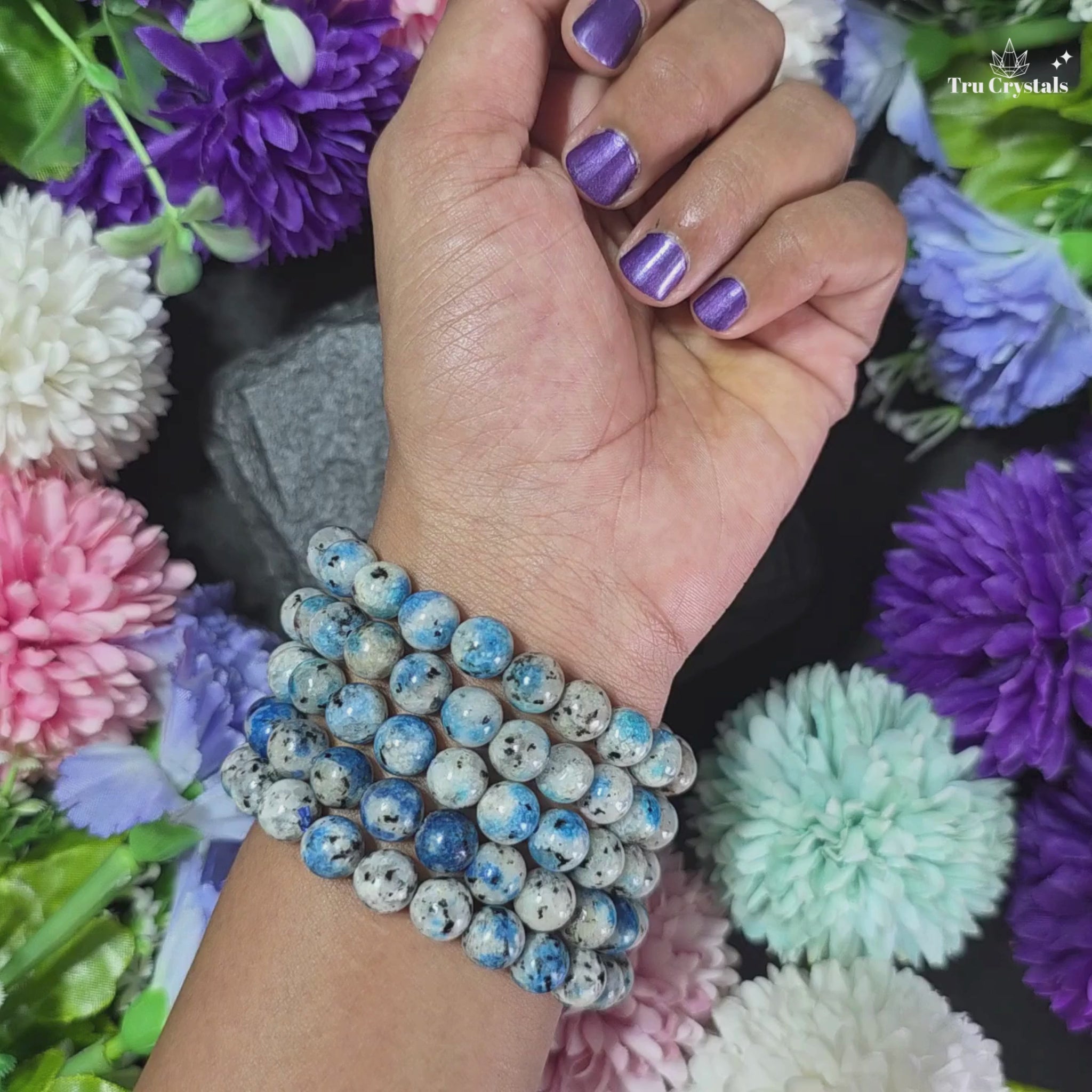 K2 Jasper bracelet placed on a wrist, surrounded by colorful flowers.