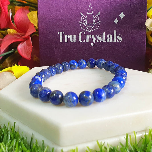 A Lapis Lazuli bracelet displayed on a white stone surface with a colorful floral background. 