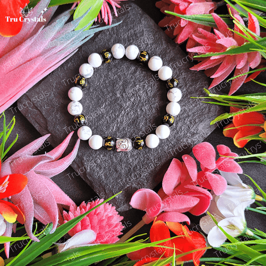 A multicolor om mani padme hum bracelet with black obsidian and howlite stones, featuring a tiny Buddha charm, displayed on a flower-decorated surface.