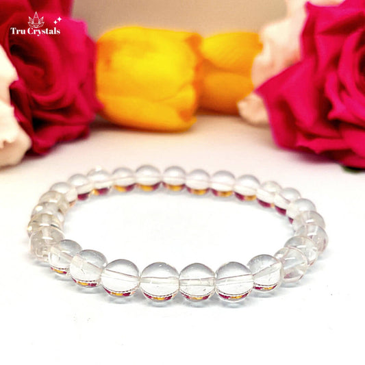 A clear quartz bracelet placed on a natural stone with a floral background, accompanied by a certification card.